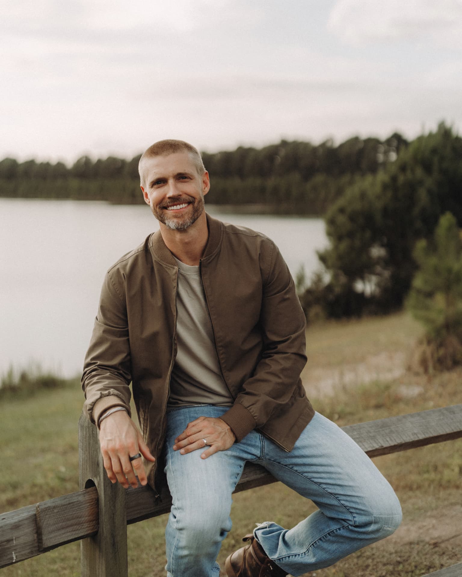Jason Blydell seated on a wooden fence by the water